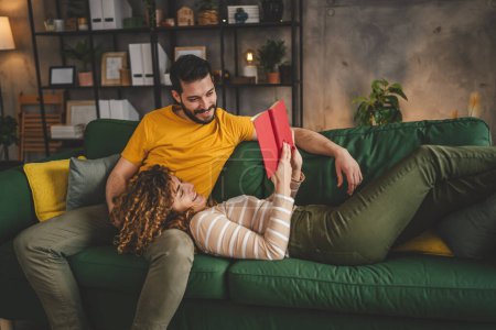 Téléchargez les photos : Homme et femme caucasien adulte couple lire des livres à la maison sur canapé-lit - en image libre de droit