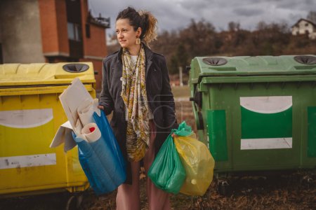 Photo for One adult woman stand with green yellow and blue bags in front of recycle containers for glass, paper and plastic zero waste eco concept - Royalty Free Image