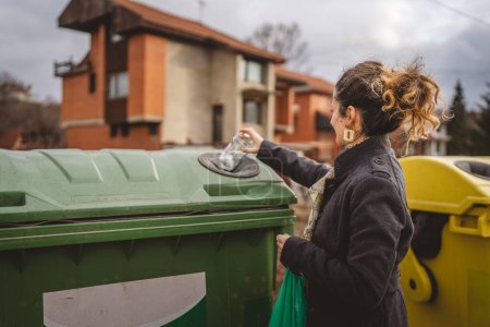 Foto de Una mujer adulta de pie con residuos de vidrio y bolsas verdes en frente de contenedores de reciclaje lanzando frasco de botella para la reutilización de residuos cero concepto ecológico - Imagen libre de derechos