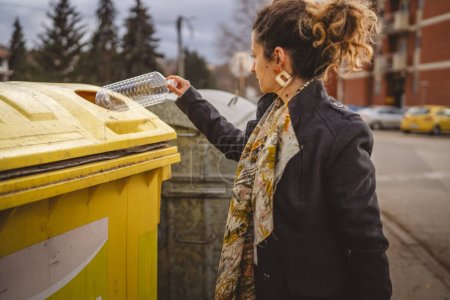 Téléchargez les photos : Une femme adulte se tient debout avec des déchets plastiques et des sacs jaunes devant des conteneurs de recyclage jetant bouteille pour la réutilisation zéro déchets concept écologique - en image libre de droit