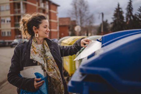 Foto de Una mujer adulta de pie con residuos de papel y bolsas azules en frente de contenedores de reciclaje lanzando para la reutilización de residuos cero concepto ecológico - Imagen libre de derechos