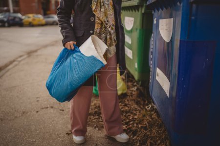 Photo for One adult woman stand with paper waste and blue bags in front of recycle containers throwing for reuse zero waste eco concept - Royalty Free Image