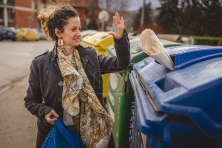 Téléchargez les photos : Une femme adulte debout avec des déchets de papier et des sacs bleus devant des conteneurs de recyclage jetant pour réutilisation zéro déchet concept écologique - en image libre de droit