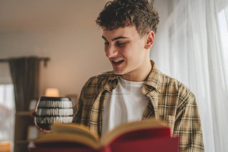 Téléchargez les photos : Jeune homme caucasien adolescent lire livre étude à la maison éducation concept - en image libre de droit