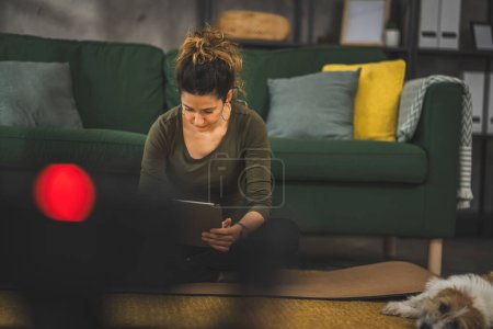Photo for One woman adult caucasian female sit on the floor at home use digital tablet for online internet search prepare for training - Royalty Free Image
