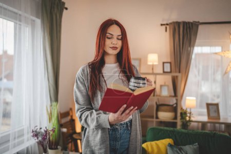 Téléchargez les photos : Jeune femme adulte une étudiante lit un livre ou étudie à la maison espace de copie de cheveux rouges - en image libre de droit