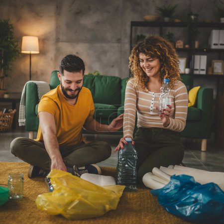 Foto de Marido y mujer mujer y hombre familia reciclar en casa clasificación de residuos de papel plástico y vidrio a verde, amarillo y azul bolsas concepto de vida sostenible - Imagen libre de derechos