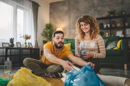 Téléchargez les photos : Mari et femme femme femme et homme famille recycler à la maison trier les déchets de papier plastique et de verre en sacs verts, jaunes et bleus concept de vie durable - en image libre de droit