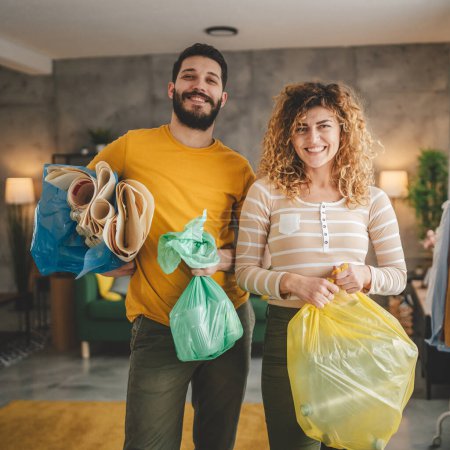 Photo for Husband and wife woman and man family recycle at home sorting waste plastic paper and glass to green, yellow and blue bags sustainable living concept - Royalty Free Image
