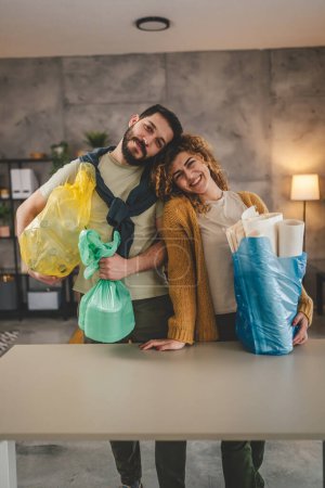 Téléchargez les photos : Mari et femme femme femme et homme famille recycler à la maison trier les déchets de papier plastique et de verre en sacs verts, jaunes et bleus concept de vie durable - en image libre de droit