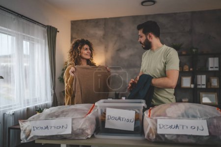 Photo for Husband and wife man and woman couple stand at home choose clothes for donation sorting wardrobe to the boxes in their apartment living room - Royalty Free Image