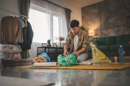 Téléchargez les photos : Un homme jeune adulte recycler à la maison trier les déchets de papier plastique et de verre - en image libre de droit