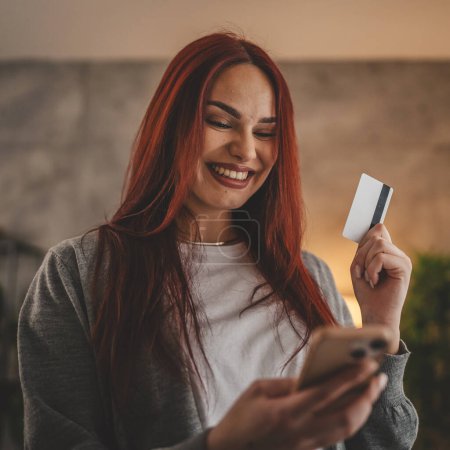 Foto de Mujer joven caucásico hembra celebrar tarjeta de crédito en línea de compras en casa - Imagen libre de derechos