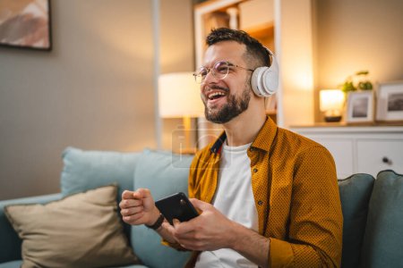 Téléchargez les photos : Un homme adulte tenir smartphone téléphone mobile à la maison sourire heureux chanter - en image libre de droit