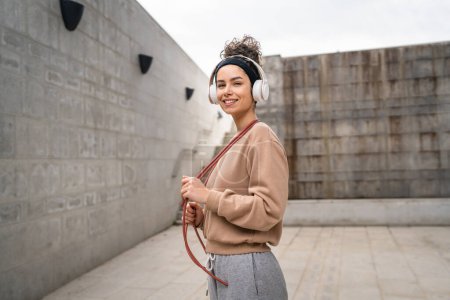 Photo for One woman young adult caucasian female jumping rope training concept beautiful sporty generation Z in day outdoor with headphones on her head copy space real person - Royalty Free Image