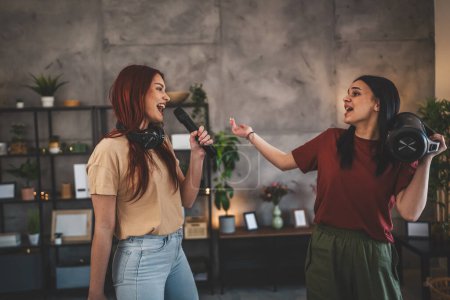 Photo for Two women young caucasian friends or sisters have fun at home females dance and sing karaoke hold microphone listen to the music happy smile joyful rhythm real people copy space - Royalty Free Image