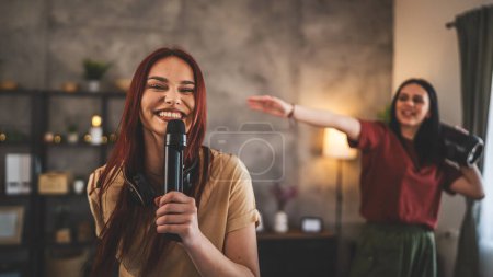 Téléchargez les photos : Deux femmes jeunes amis caucasiens ou sœurs s'amusent à la maison femmes dansent et chantent karaoké tenir microphone écouter la musique sourire heureux rythme joyeux vraies personnes copier l'espace - en image libre de droit