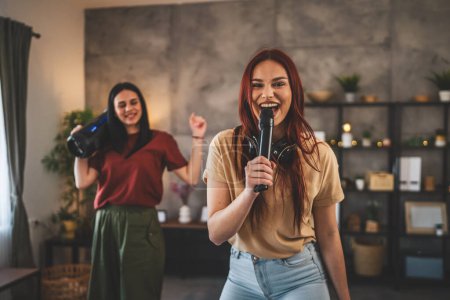 Foto de Dos mujeres jóvenes caucásicos amigos o hermanas se divierten en casa hembras bailan y cantan karaoke celebrar micrófono escuchar la música sonrisa feliz ritmo alegre gente real copiar espacio - Imagen libre de derechos