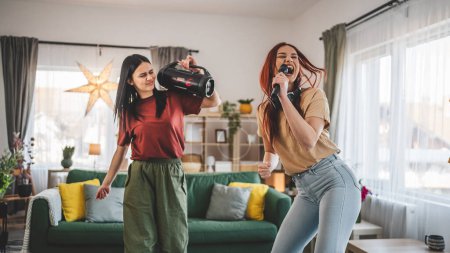 Foto de Dos mujeres jóvenes caucásicos amigos o hermanas se divierten en casa hembras bailan y cantan karaoke celebrar micrófono escuchar la música sonrisa feliz ritmo alegre gente real copiar espacio - Imagen libre de derechos