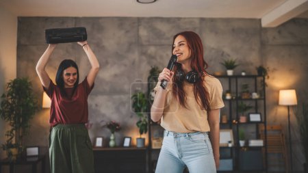 Téléchargez les photos : Deux femmes jeunes amis caucasiens ou sœurs s'amusent à la maison femmes dansent et chantent karaoké tenir microphone écouter la musique sourire heureux rythme joyeux vraies personnes copier l'espace - en image libre de droit