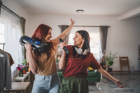 Photo for Two women young caucasian friends or sisters have fun at home females dance and sing karaoke hold microphone listen to the music happy smile joyful rhythm real people copy space - Royalty Free Image