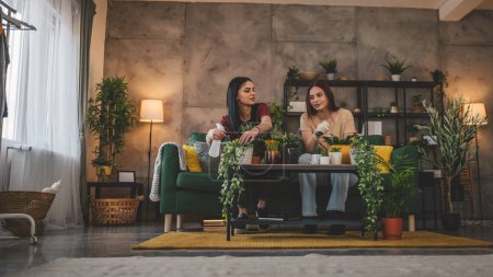 Téléchargez les photos : Deux femmes caucasiennes amis ou sœurs plantent des fleurs ensemble en prenant soin de plantes à la maison personnes réelles concept de famille de la vie familiale - en image libre de droit