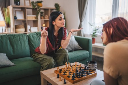 Foto de Dos mujeres jóvenes hermanas amigas jugar ajedrez juego de mesa en casa - Imagen libre de derechos