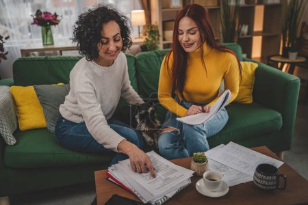 Photo for Two women young caucasian female student sit at home with her mentor professor looking to the textbook explaining lesson study prepare for exam learning education concept real people copy space - Royalty Free Image