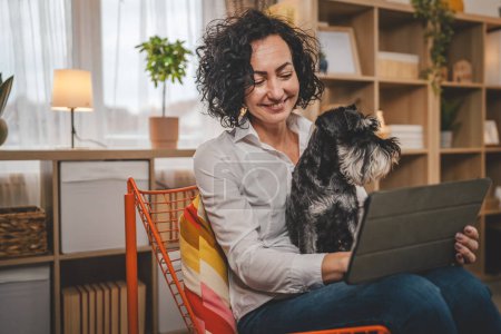 Téléchargez les photos : Portrait femme caucasienne adulte utiliser tablette numérique avec chien de compagnie à la maison - en image libre de droit