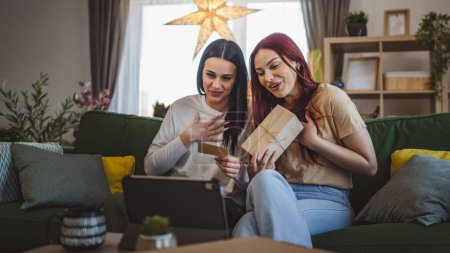Téléchargez les photos : Deux adolescentes amies ou sœurs reçoivent des cadeaux en boîte ouverte carte de lecture heureux sourire devant tablette numérique à la maison appel vidéo en ligne - en image libre de droit