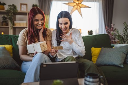Téléchargez les photos : Deux adolescentes amies ou sœurs reçoivent des cadeaux en boîte ouverte carte de lecture heureux sourire devant tablette numérique à la maison appel vidéo en ligne - en image libre de droit