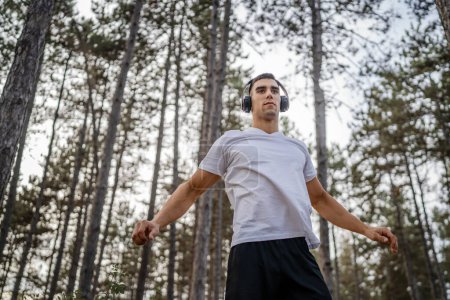 Téléchargez les photos : Un homme jeune athlète homme caucasien étirement dans les bois dans la nature en plein air jogging ou exercice en automne ou en été jour sport fitness et loisirs mode de vie sain concept personnes réelles copier l'espace - en image libre de droit