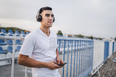 Photo for Portrait of an athlete using mobile phone during morning run Athletic man listening to music on headphones use mobile phone app application - Royalty Free Image