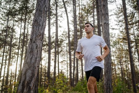 Téléchargez les photos : Un homme jeune athlète homme caucasien courir à travers les bois dans la nature jogging en plein air en automne ou en été jour sport fitness et loisirs mode de vie sain concept personnes réelles copier l'espace - en image libre de droit