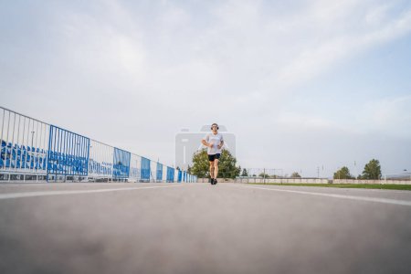 Photo for Adult caucasian man jogging on the running track male athlete in stadium training run in sunny spring or summer day real people healthy lifestyle concept - Royalty Free Image