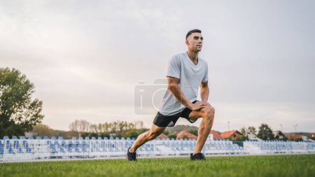 Téléchargez les photos : Un homme jeune athlète masculin caucasien étirer en plein air au stade piste de jogging ou d'exercice en automne ou en été jour sport fitness et loisirs mode de vie sain concept personnes réelles copier l'espace - en image libre de droit