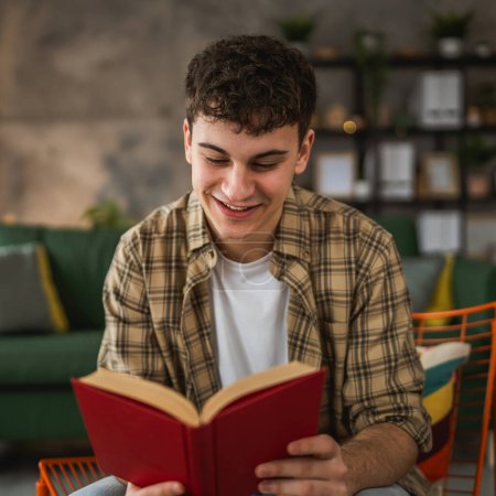 Téléchargez les photos : Jeune homme caucasien adolescent lire livre étude à la maison éducation concept - en image libre de droit