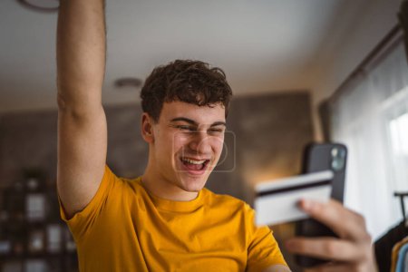 Téléchargez les photos : Adolescent jeune homme à la maison utilisation carte de crédit achats en ligne - en image libre de droit