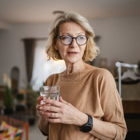 Téléchargez les photos : Gros plan portrait d'une femme mature avec un verre d'eau à la maison - en image libre de droit