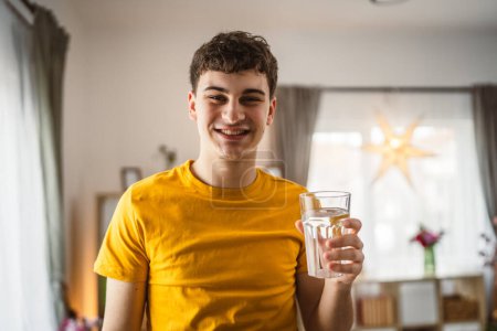 Téléchargez les photos : Homme jeune caucasien mâle tenir verre d'eau à la maison - en image libre de droit
