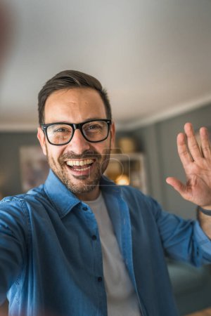 Téléchargez les photos : Un homme adulte portrait de caucasien mâle avec barbe et lunettes se tenir à la maison heureux sourire copie espace autoportrait selfie - en image libre de droit