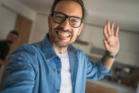 Téléchargez les photos : Un homme adulte portrait de caucasien mâle avec barbe et lunettes se tenir à la maison heureux sourire copie espace autoportrait selfie - en image libre de droit
