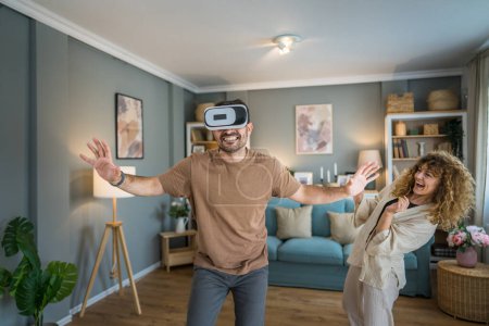 Photo for Man mature adult caucasian male husband with his wife or girlfriend couple at home enjoy virtual reality VR headset with googles on the head have fun modern technology leisure concept copy space - Royalty Free Image
