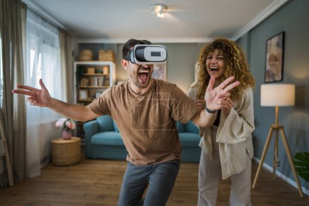 Photo for Man mature adult caucasian male husband with his wife or girlfriend couple at home enjoy virtual reality VR headset with googles on the head have fun modern technology leisure concept copy space - Royalty Free Image