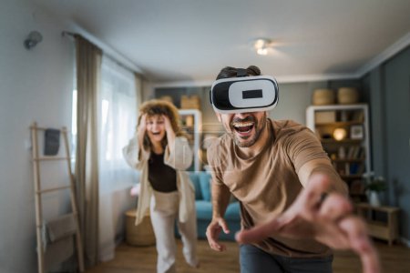 Téléchargez les photos : Homme mature adulte caucasien mâle mari avec sa femme ou sa petite amie couple à la maison profiter de la réalité virtuelle VR casque avec googles sur la tête avoir amusant moderne technologie loisirs concept copier espace - en image libre de droit