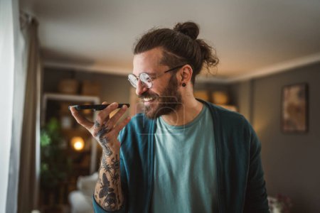 Photo for One adult modern man with eyeglasses beard and long hair stand at home use mobile phone talk - Royalty Free Image