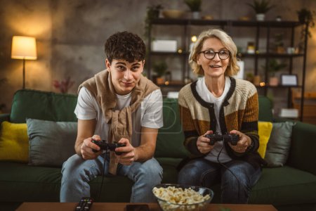 Téléchargez les photos : Adolescent mâle et sa mère mature femme homme jouer console jeu vidéo - en image libre de droit