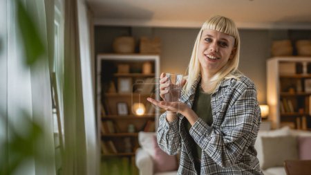 Photo for One woman beautiful blonde young adult female modern haircut at home with glass of water - Royalty Free Image