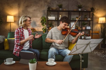 Photo for Young man learn how to play violin under instruction of mature woman female professor tutor at home take private class - Royalty Free Image