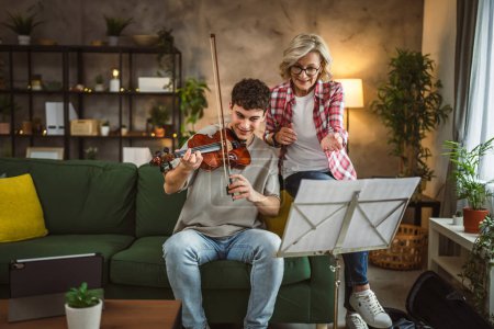 Photo for Young man learn how to play violin under instruction of mature woman female professor tutor at home take private class - Royalty Free Image